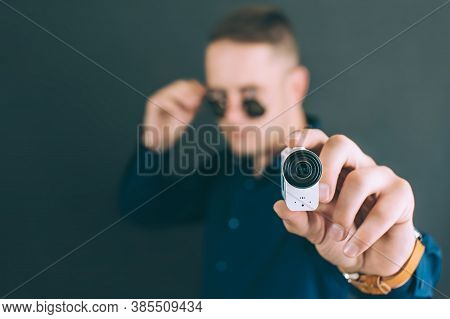 The Guy Takes Photos, Videos With An Action Camera, With One Hand. On A Black Background In The Stud