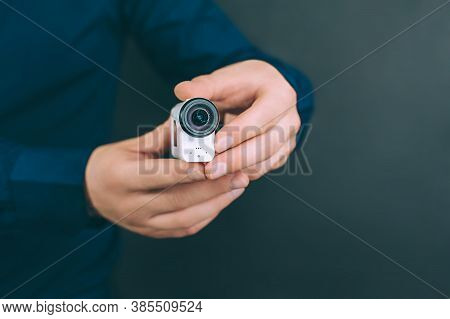 White Action Video Camera, In The Hands Of A Guy On A Black Background In The Studio.