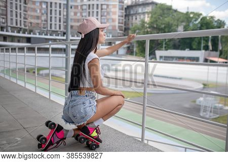 Dark-haired Girl In Jeans Shorts Sitting On Her Hunkers
