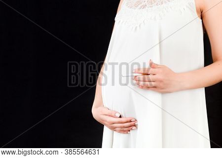 Close Up Of Pregnant Woman In White Dress With A Cigarette Against Her Belly At Black Background. Da
