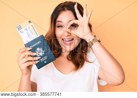 Young beautiful caucasian woman holding boarding pass and passport smiling happy doing ok sign with hand on eye looking through fingers 