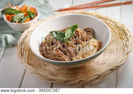 Japanese soup with Enoki mushrooms, soba noodles, spinach, carrot, and soy sauce on the willow tray