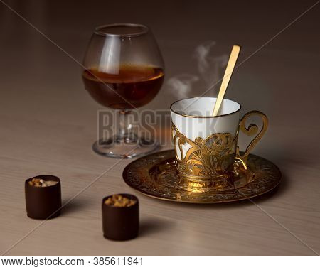 Cognac In A Tulip-shaped Glass, A Golden Coffee Cup, A Spoon, Chocolate On The Table, Luxurious Eleg