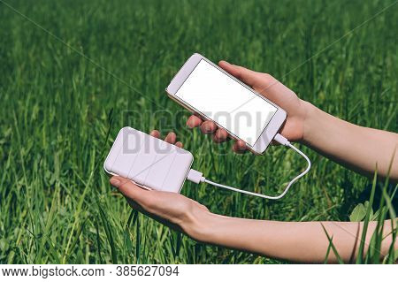 Mock-up Of A Smartphone And A Power Bank In The Girl's Hand. Against The Background Of A Field With