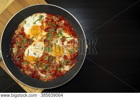 Shakshuka - Poached Eggs In Tomato Sauce, Onion, Pepper And In Iron Pan On Dark Wooden Table With Co