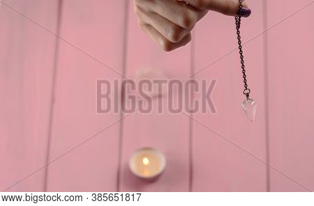 Arm Of A Dowser With Hand-held Pendulum On A Chain With A Natural Crystal On A Background Of Pink Wo
