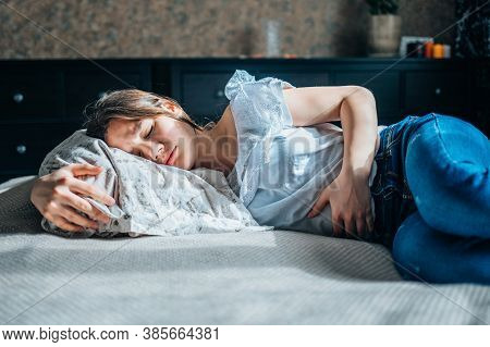 Young Woman Suffering From Abdominal Pain Lying On A Bed At Home.