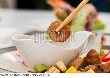 Close Up Of Chopsticks Holding Namnueng Piece While Dip Sauce In White Bowl