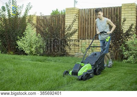 A Teenager Mows The Lawn With A Lawn Mower.