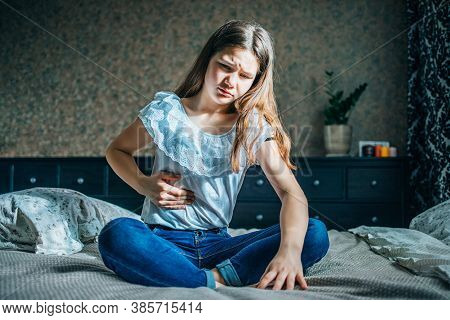 Young Brunette Sits On A Bed In Her Room, Holds A Sick Stomach With Her Hand, Horizontal Shot, Selec
