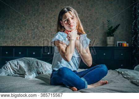 A Young Brunette Girl Sits On A Bed In Her Room, She Has A Sore Throat, She Squeezes Her Neck With H