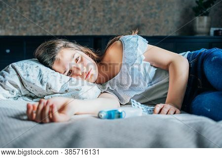 A Sad Young Girl Is Lying On A Bed In Her Room. Her Eyes Are Open. Next To Her Is A Thermometer And 