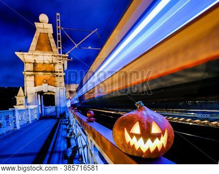 Halloween Pumpkin With A Glowing Grimace At Night On The Railway Bridge. In The Background There Are