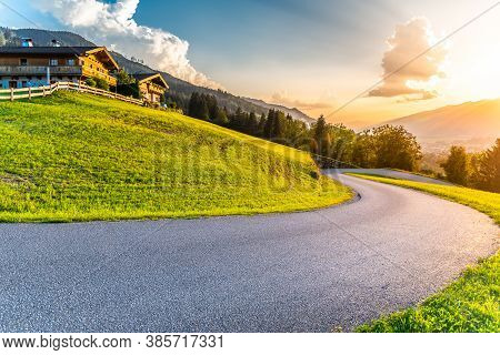 Romantic Sunset In The Mountains. Alpine Rural Curvy Road, Green Meadows And High Peaks Of Austrian 