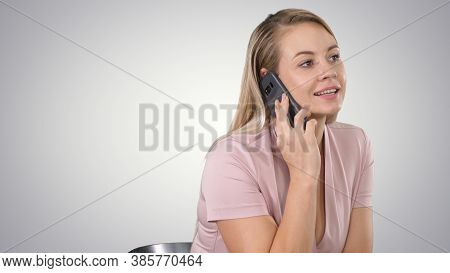Portrait Of Smiling Young Woman Making A Call Sitting On Gradien