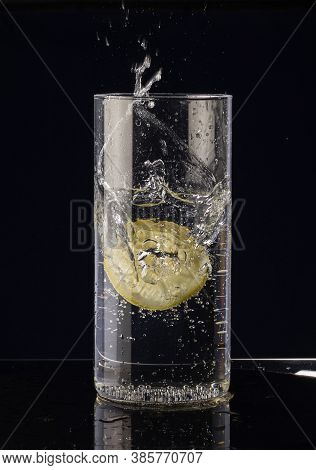 A Slice Of Lemon Falls Into A Glass Of Water On A Black Background.