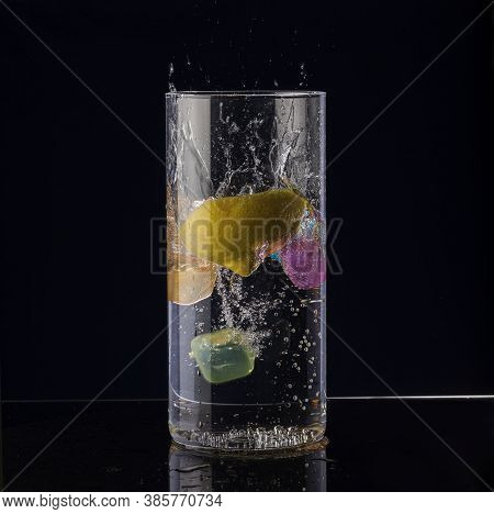 A Slice Of Lemon Falls Into A Glass Of Water On A Black Background.