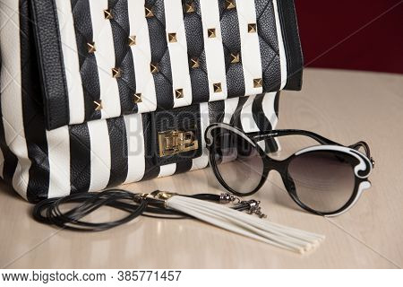 Two-color sunglasses and modern bag on the table in the room, elegant life style concept