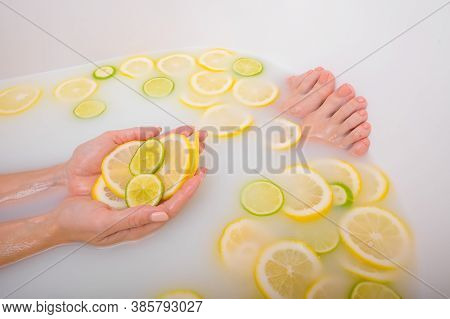 Faceless Beautiful Young Woman Takes A Bath With Milk Lemons And Lime. Cropped Photo. Close-up Of Fe