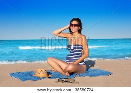 Bella donna incinta seduta sulla spiaggia blu sabbia nelle vacanze estive