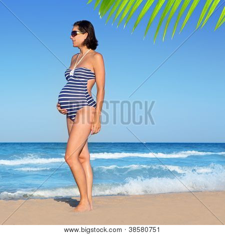 Bella donna incinta in piedi sulla spiaggia blu in vacanza estiva