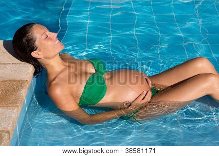 Abbronzatura bella donna incinta rilassati nella piscina blu con bikini verde