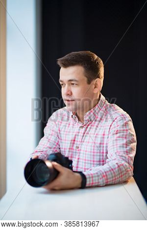 A Male Photographer In A Checkered Shirt Sits At A Table And Holds A Camera In His Hands. Creative P