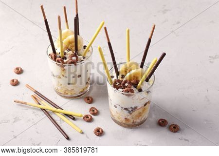 Dessert In Glasses With Chocolate, Granola And Banana, Decorated With Sticks Pocky On Gray Backgroun
