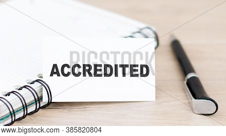 Card With Accredited Text On Green Wooden Background Next To Notepad And Pen
