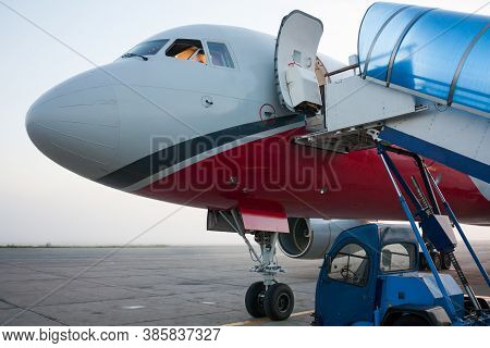 Front Of The Passenger Airplane With Open Door And Jetway Ramp Near