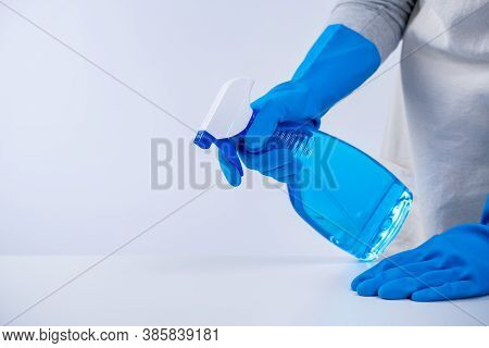 Young Woman Housekeeper In Apron Is Cleaning, Wiping Down Table Surface With Blue Gloves, Wet Yellow