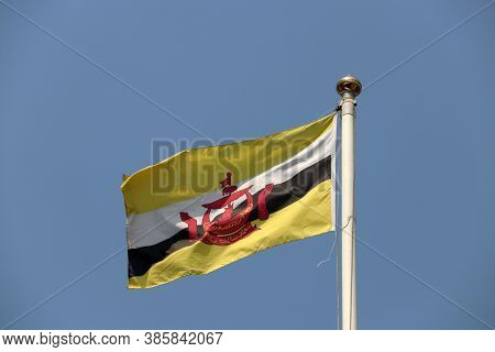 National Flag Of Brunei On Bright Blue Sky Background. Blown Away By Wind. Brunei Is One Of The Ten 