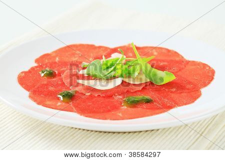 skivad carpaccio med pesto och rucolla på den vita plattan