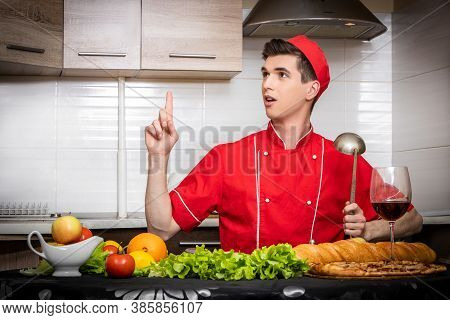 Young Man Chef In Red Uniform Holding Index Finger Up And Ladle With Great New Idea On Light Backgro