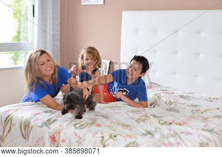 Mom Plays With Two Kids With A Dog In The Bedroom On The Bed.spending Time At Home With Family.takin