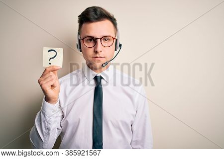 Young call center operator man wearing headset holding paper note with question mark with a confident expression on smart face thinking serious