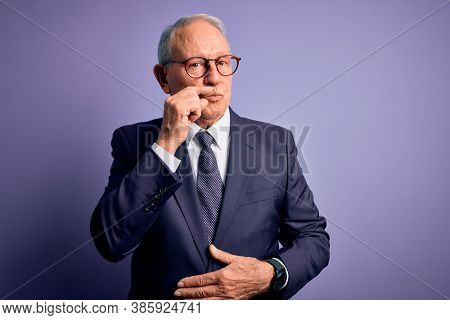 Grey haired senior business man wearing glasses and elegant suit and tie over purple background mouth and lips shut as zip with fingers. Secret and silent, taboo talking