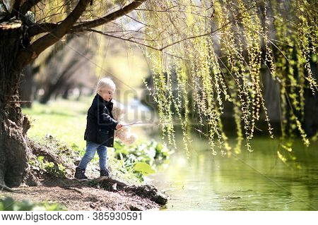 Little Boy By The River. He Is Holding A Teddy Bear In His Hands