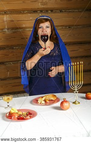 On The Eve Of Rosh Ashana, A Jewish Woman Stands At A Festive Table With Burning Candles With A Glas