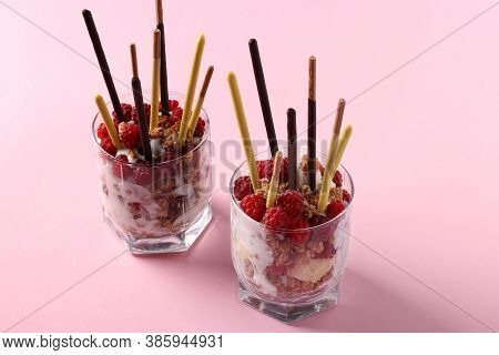 Two Glasses With Chocolate Granola, Banana And Raspberry, Decorated With Sticks Pocky On Pink Backgr