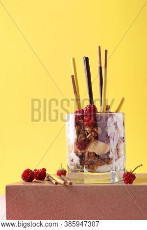 Dessert In Glass With Chocolate Granola, Banana And Raspberry, Decorated With Sticks Pocky On Pink A