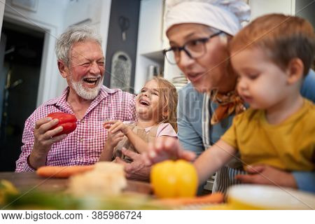 caucasian grandparents having fun with their grandchildren in the kitchen playing with vegetebles