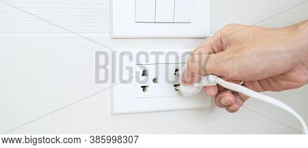 Closeup Male Finger Unplugging Or Plugging Of Electricity Device On White Wall At Home. Energy Savin