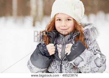 Closeup portret van meisje in grijze jas met bont kraag en gebreide muts in besneeuwde park