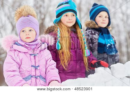 Meisje en twee oudere kinderen staan achter de muur van sneeuw blokken, focus op meisje