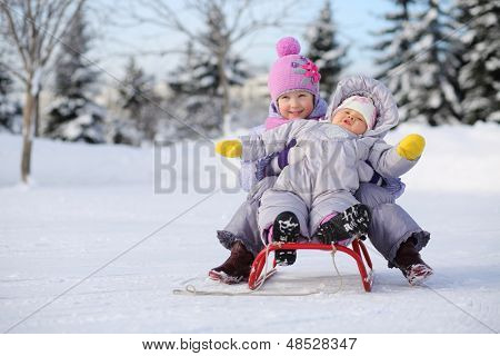 Menina, bebê, vestido com roupas quentes, perto de floresta sente-se no trenó vermelho no inverno.