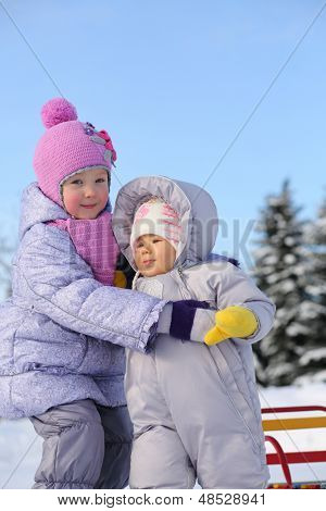 Irmã mais velha abraços bebê vestido com roupas quentes ao ar livre no inverno.