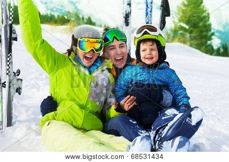Happy parents and boy with ski masks sit on snow