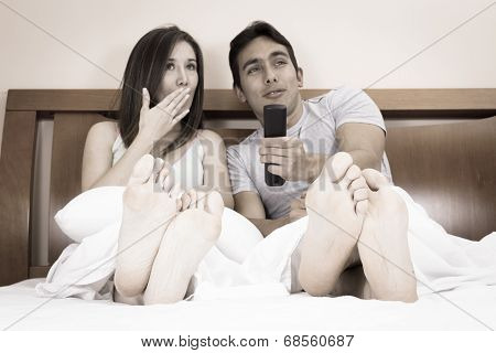 cute couple lying in bed watching tv