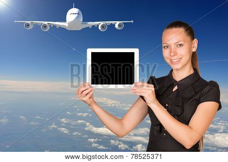 Beautiful businesswoman holding tablet PC. Blue sky, clowds and jet airliner as backdrop